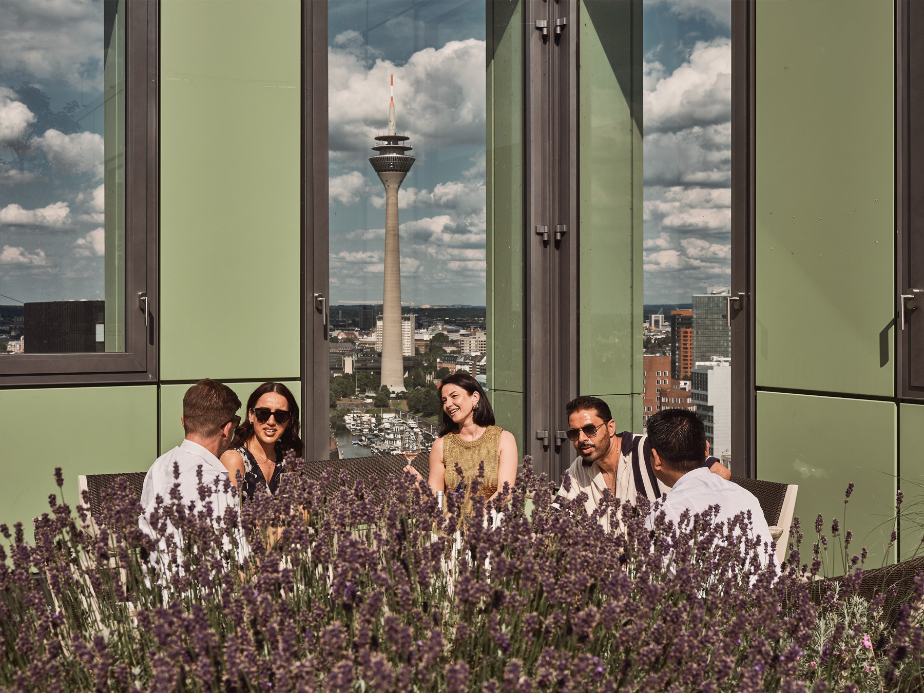 Personen genießen die Sonne auf der Dachterrasse des WIN WIN im Düsseldorfer Medienhafen mit Blick auf die Skyline und Lavendelpflanzen im Vordergrund.