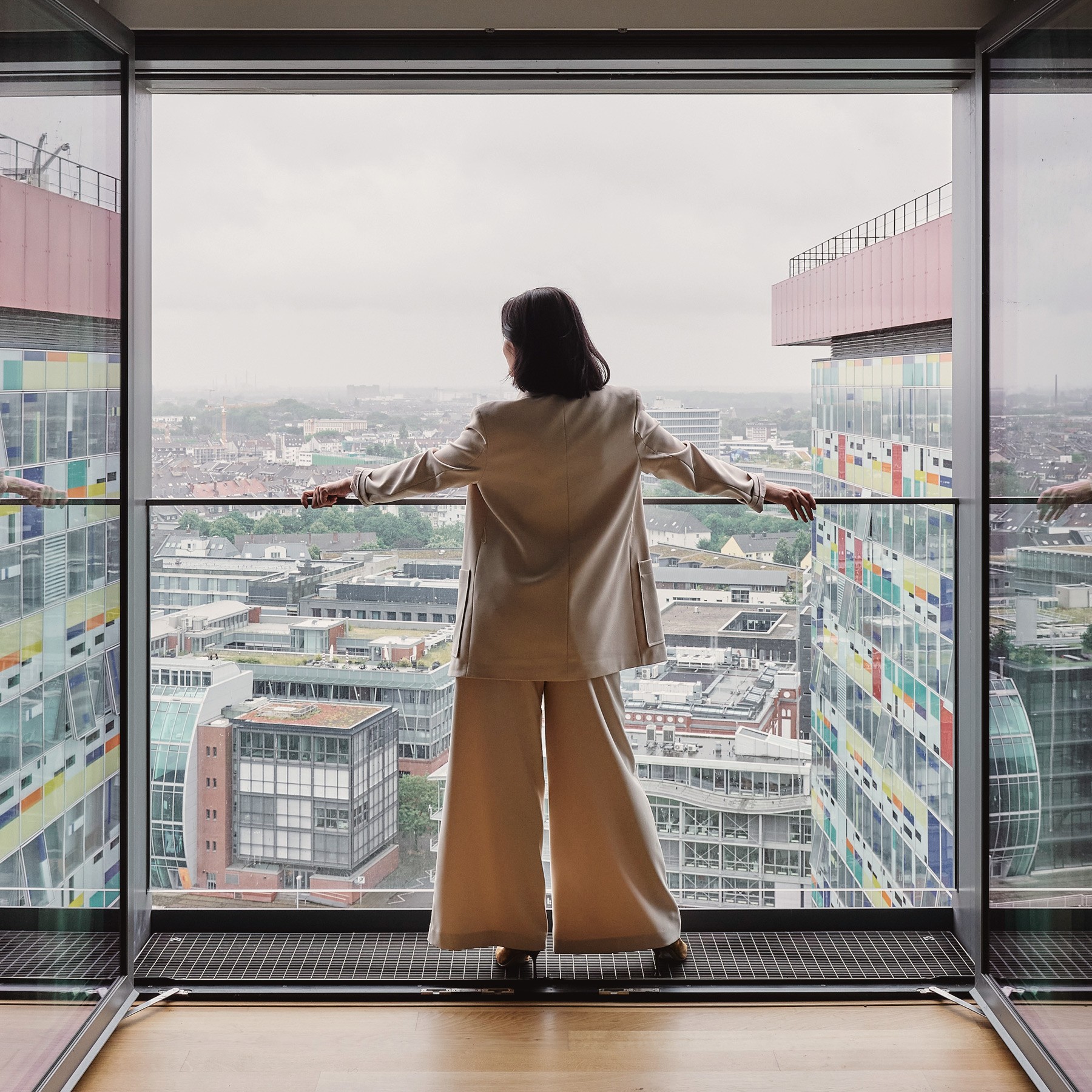 Frau steht in einer WIN WIN Wohnung im Medienhafen Düsseldorf an der geöffneten Panoramafront und blickt über die Stadt.