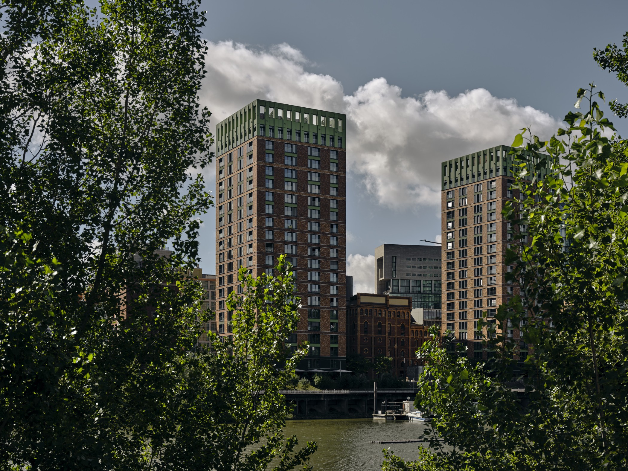 Blick auf die WIN WIN Türme im Medienhafen Düsseldorf, eingerahmt von dichter grüner Ufervegetation am Hafenbecken.