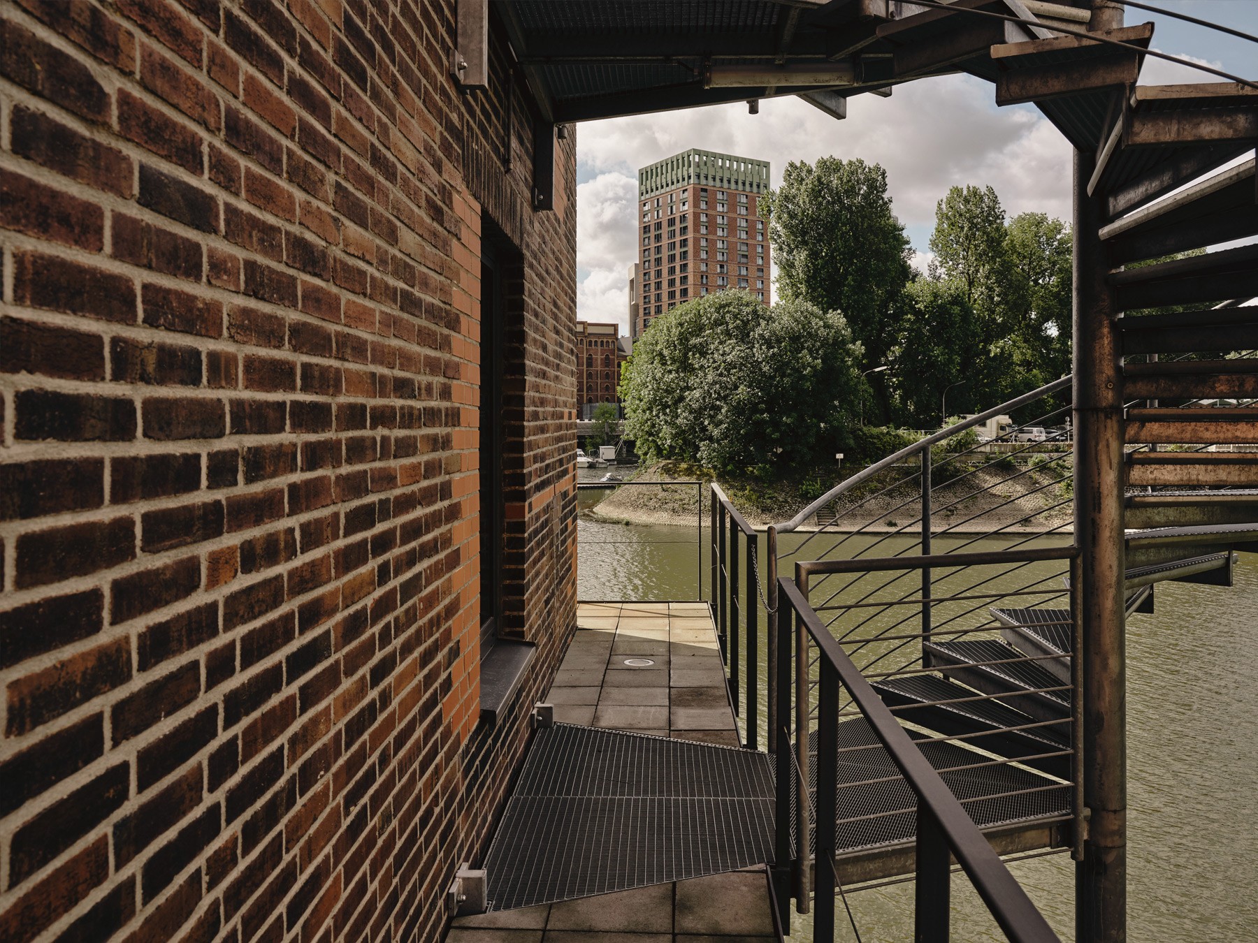 Blick auf einen WIN WIN Turm im Medienhafen Düsseldorf, eingerahmt von industriellen Stahlstrukturen und Backsteinarchitektur im Vordergrund.