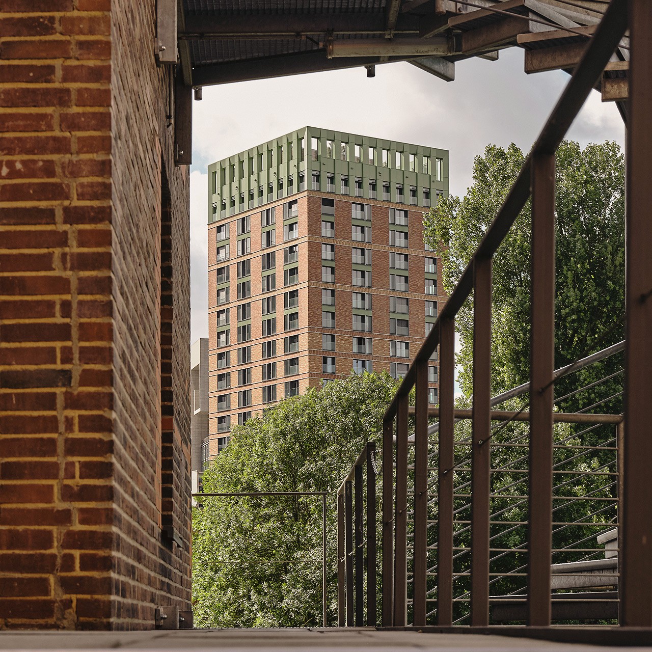 Blick auf einen WIN WIN Turm im Medienhafen Düsseldorf, eingerahmt von industriellen Stahlstrukturen und Backsteinarchitektur im Vordergrund.