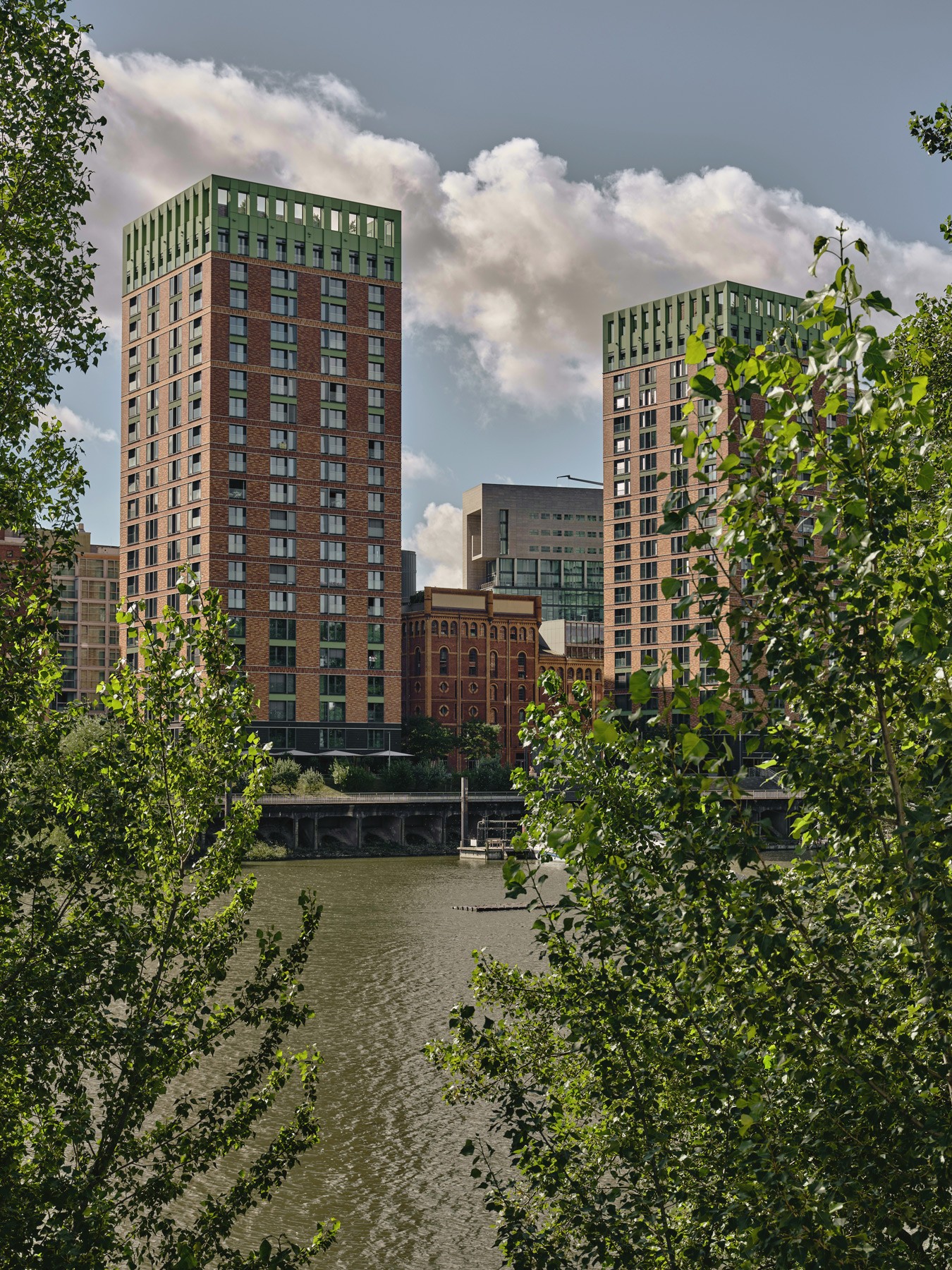 Blick auf die WIN WIN Türme im Medienhafen Düsseldorf, eingerahmt von dichter grüner Ufervegetation am Hafenbecken.