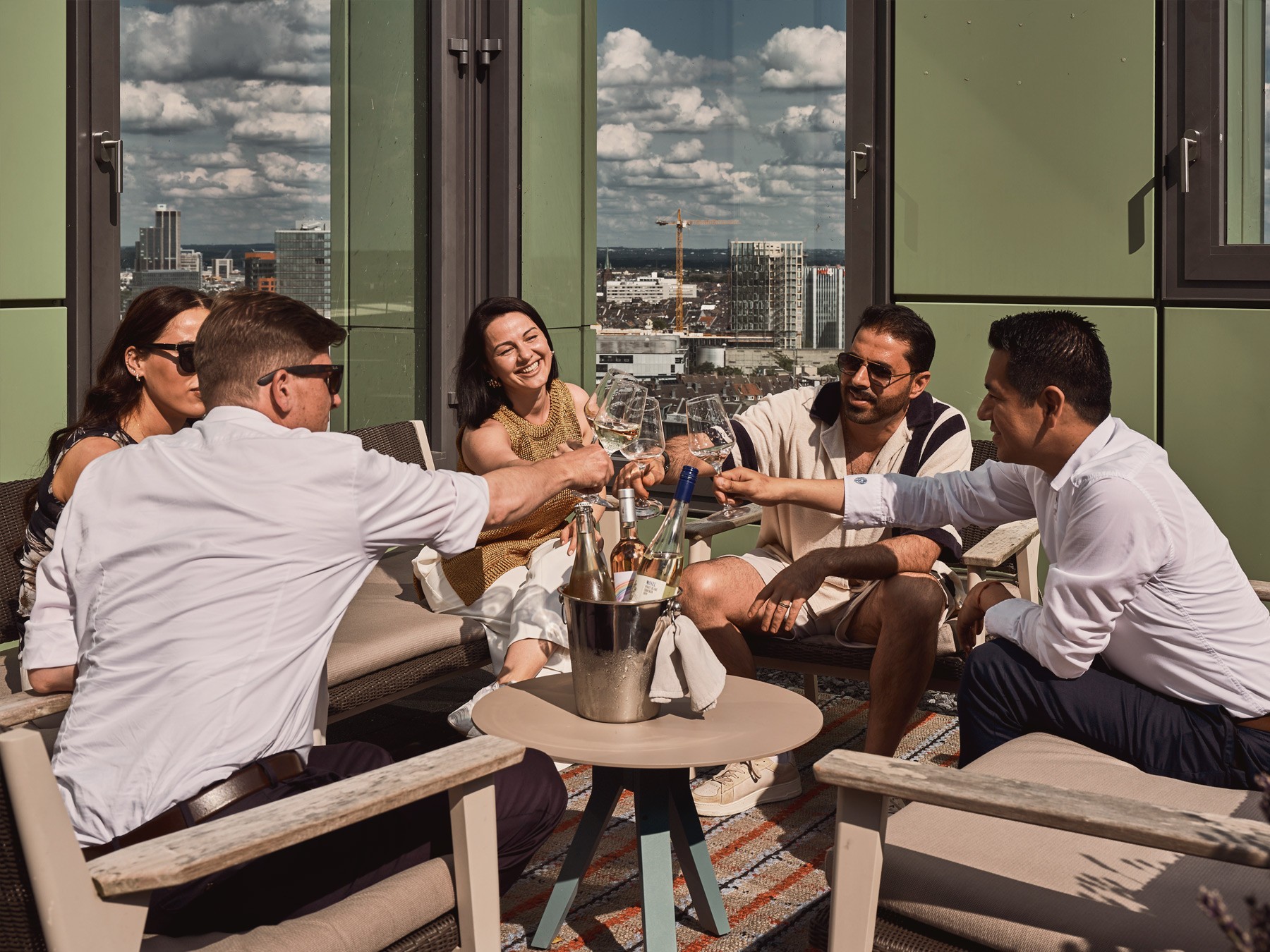Gruppe von Freunden stößt auf der Dachterrasse des WIN WIN im Medienhafen Düsseldorf mit Blick über die Stadt an.
