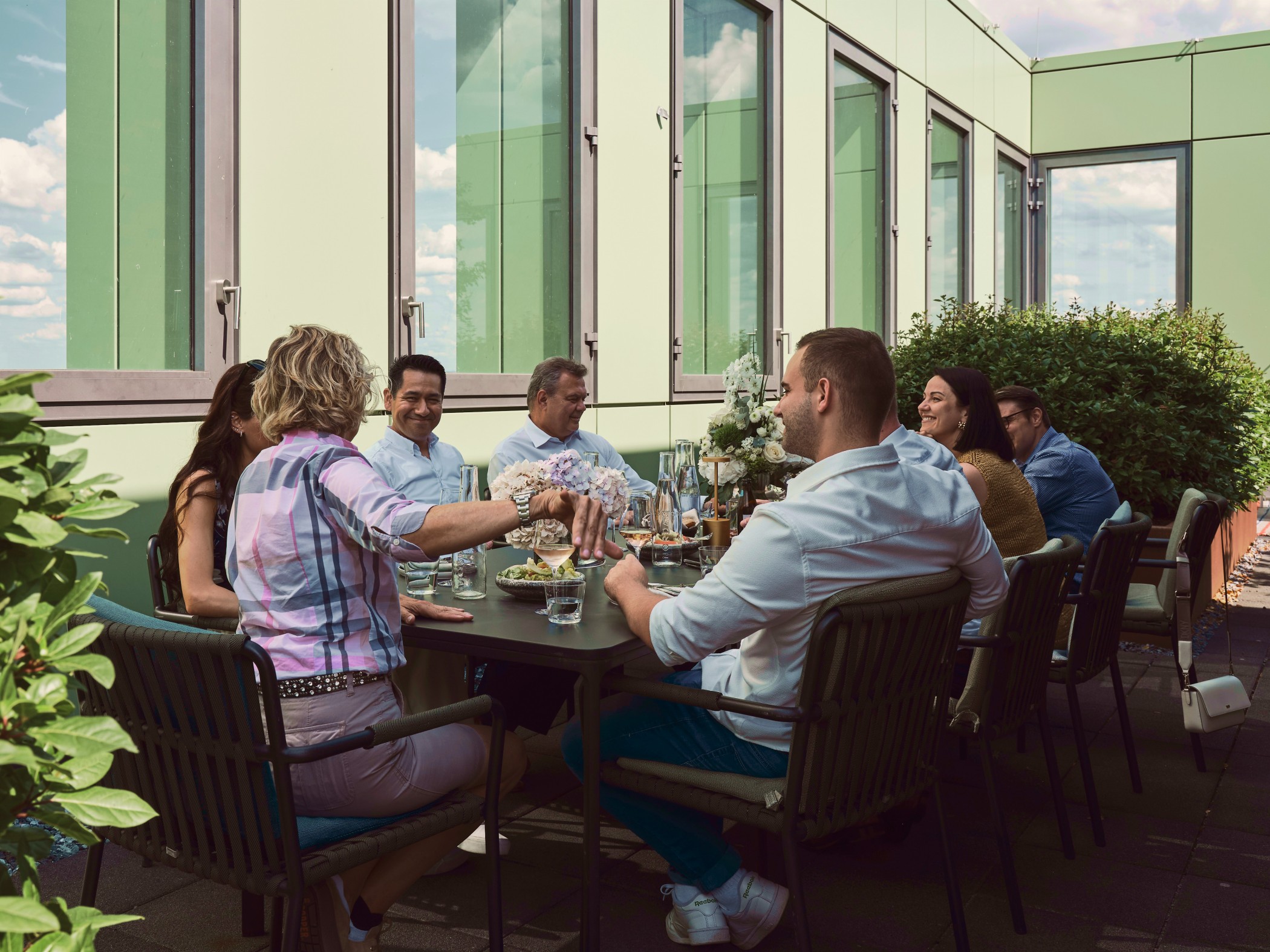Gruppe von Freunden beim gemeinsamen Essen und Anstoßen auf der begrünten Dachterrasse des WIN WIN im Medienhafn Düsseldorf