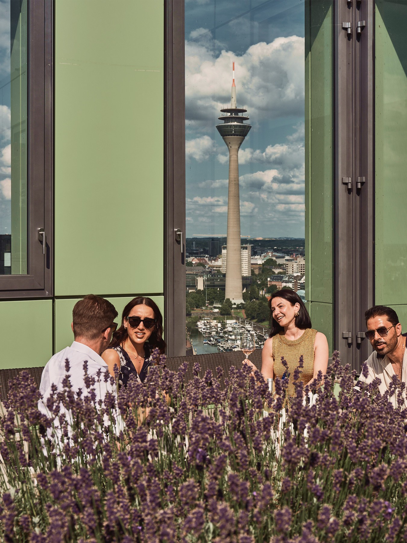 Personen genießen die Sonne auf der Dachterrasse des WIN WIN im Düsseldorfer Medienhafen mit Blick auf die Skyline und Lavendelpflanzen im Vordergrund.