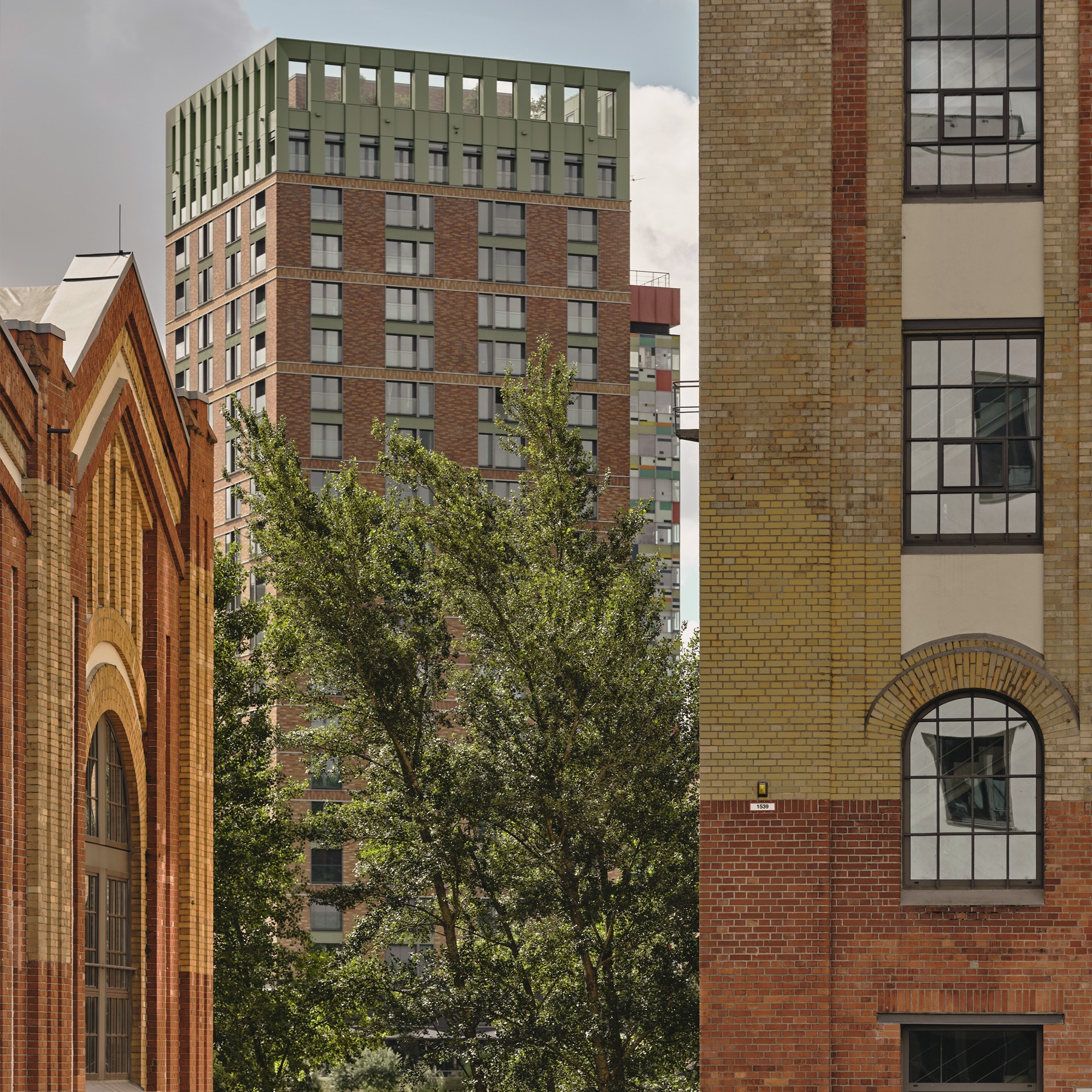 Blick auf einen WIN WIN Turm im Medienhafen Düsseldorf, eingerahmt von historischen Backsteingebäuden und grüner Vegetation im Vordergrund.