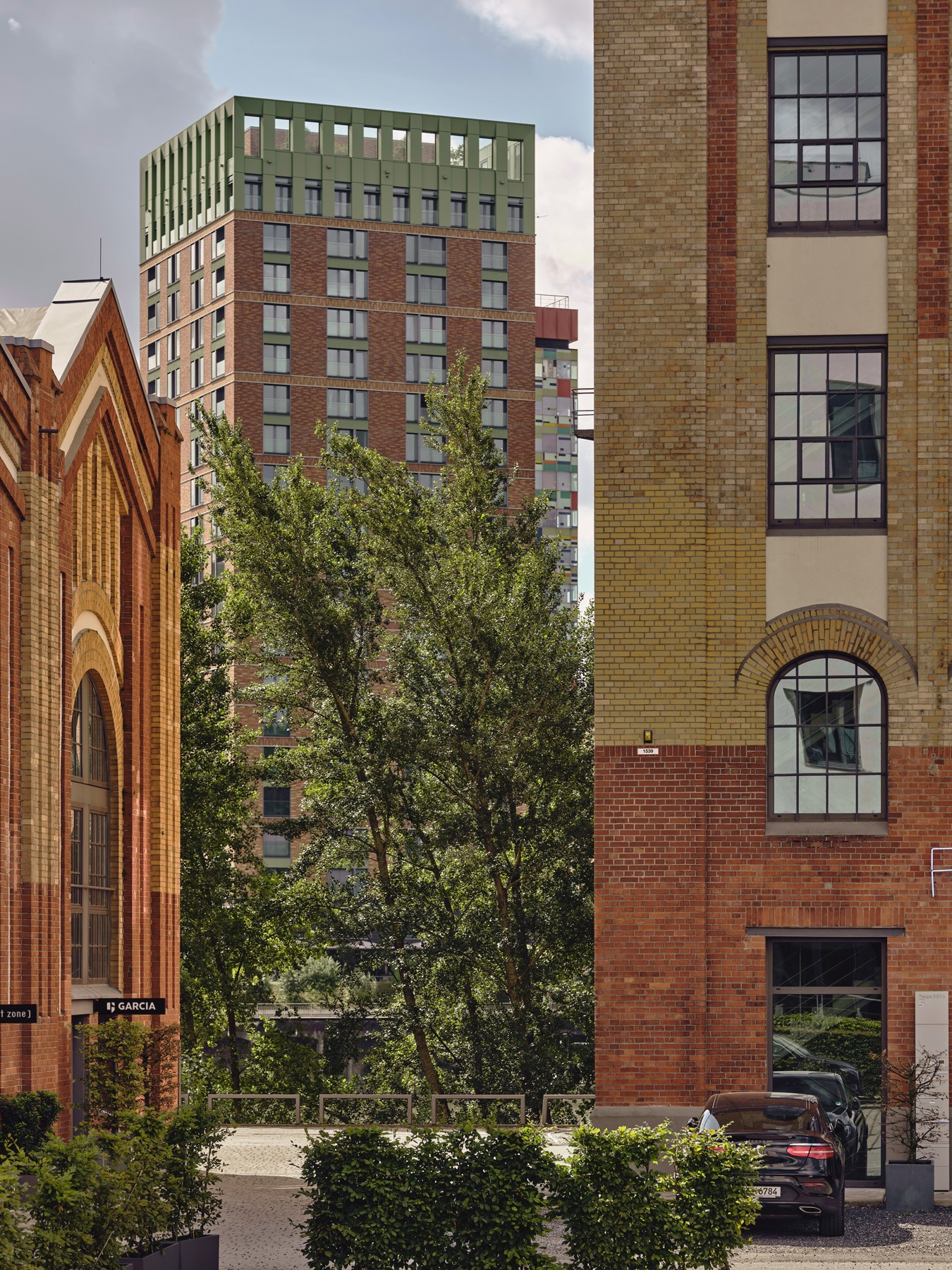 Blick auf einen WIN WIN Turm im Medienhafen Düsseldorf, eingerahmt von historischen Backsteingebäuden und grüner Vegetation im Vordergrund.