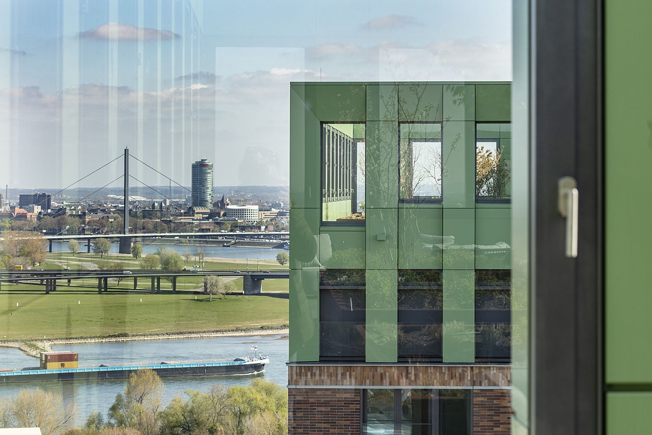 View through glass across the Rhine with a cargo ship to a cable-stayed bridge, the green rooftop structure of a WIN WIN tower on the right