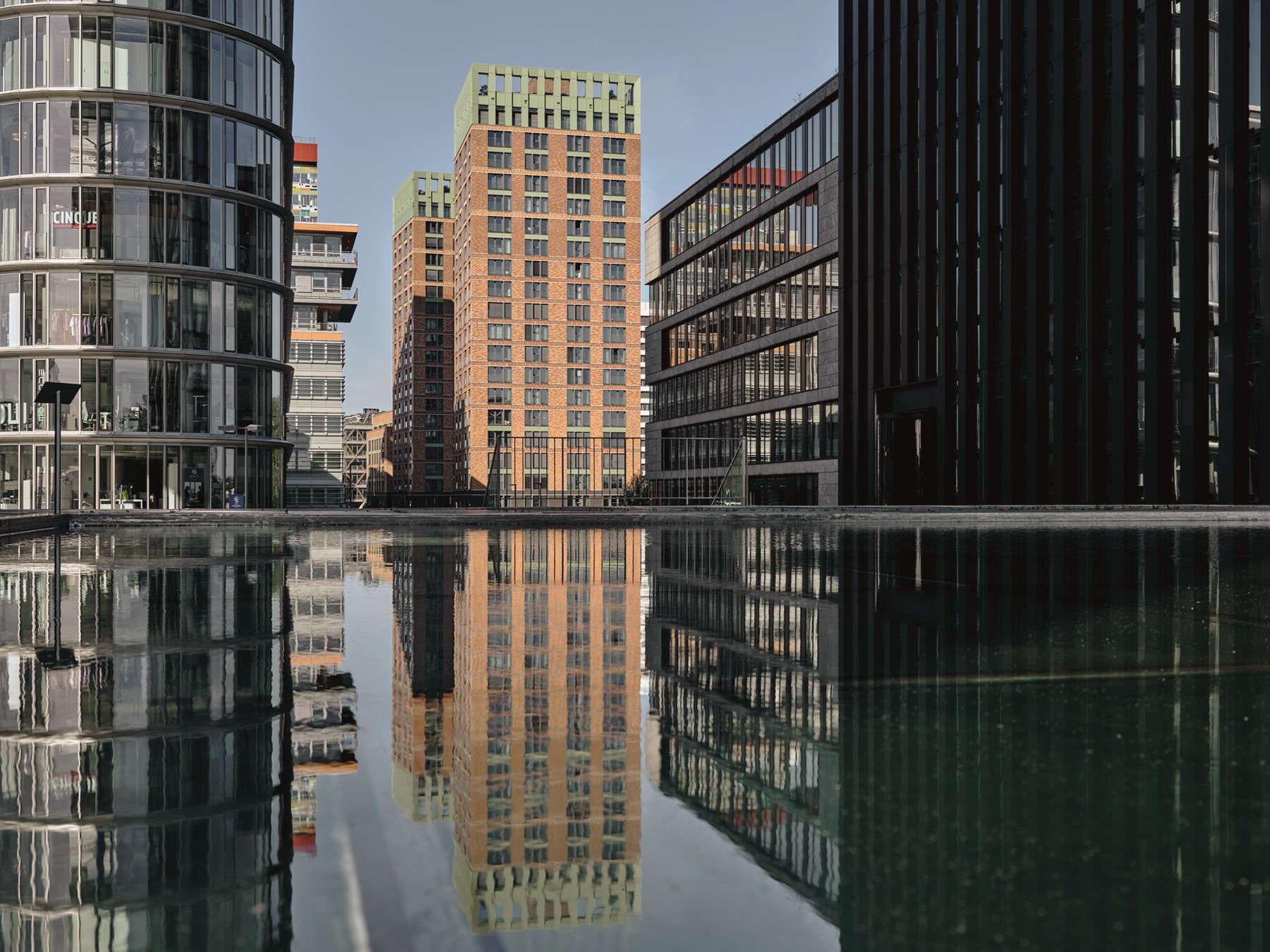 The WIN WIN towers between glass office buildings, reflected in a calm stretch of water in the Medienhafen