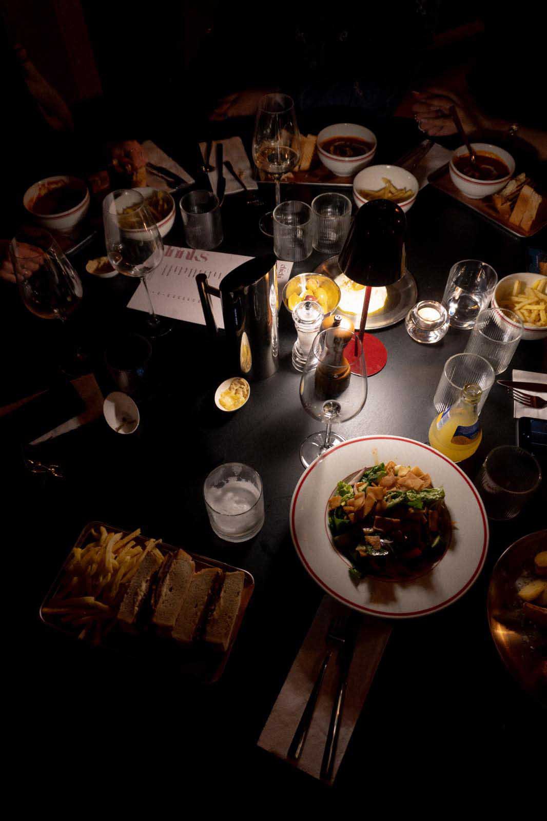 Tisch im Restaurant chichi von oben mit Salat, Sandwich, Pommes frites, Suppenschalen und Getränken bei Tischlampenlicht
