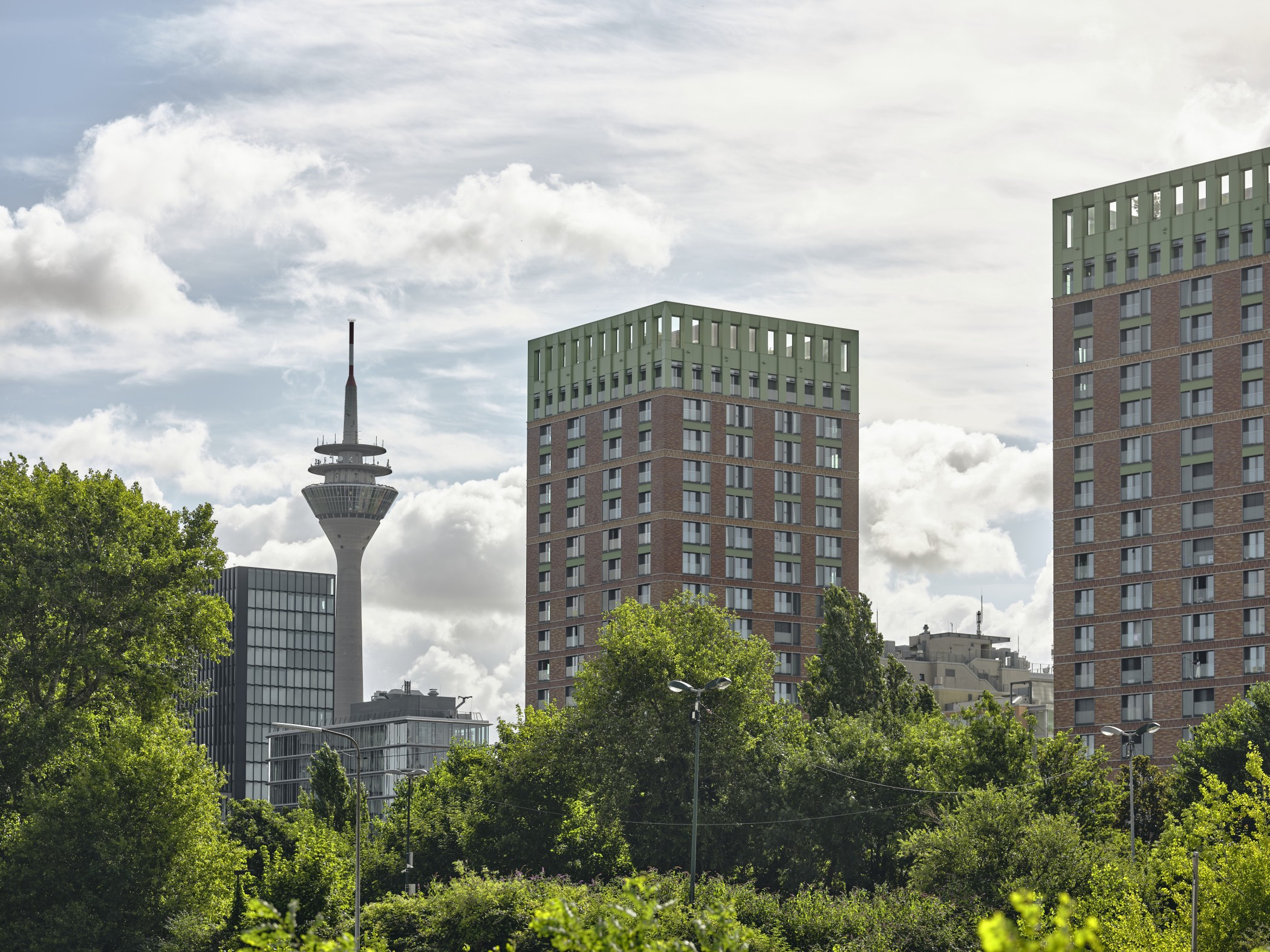 Blick auf die WIN WIN Türme im Medienhafen Düsseldorf mit dem Rheinturm im Hintergrund über einer grünen Baumlandschaft.