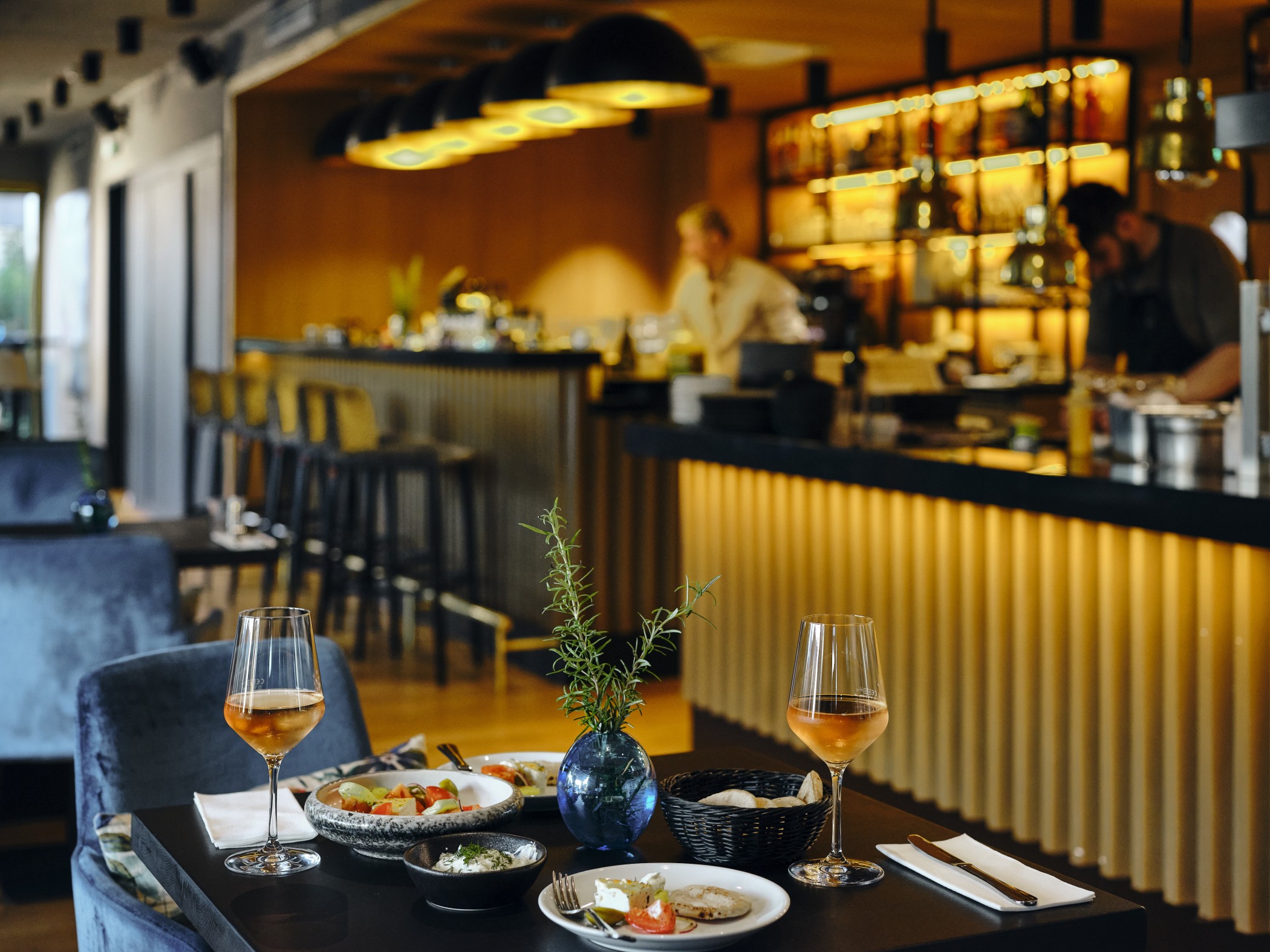 Restaurant im WIN WIN mit beleuchteter Bar, im Vordergrund ein gedeckter Tisch mit Vorspeisen und zwei Gläsern Wein