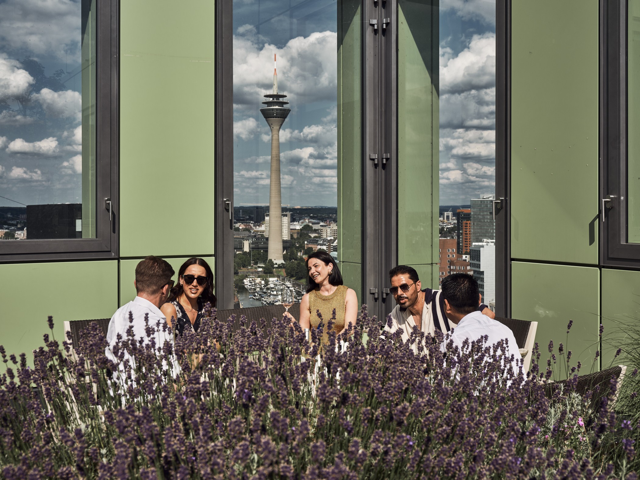 Personen genießen die Sonne auf der Dachterrasse des WIN WIN im Düsseldorfer Medienhafen mit Blick auf die Skyline und Lavendelpflanzen im Vordergrund.