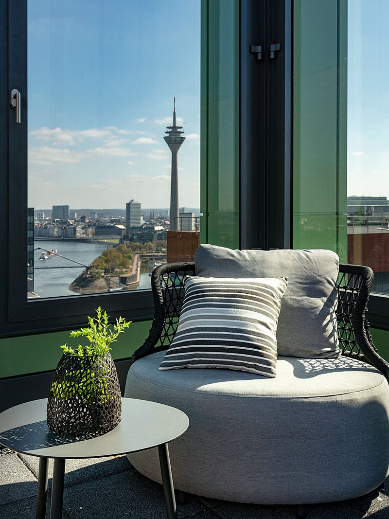 Gemütlicher Lounge-Sessel auf der Dachterrasse des WIN WIN im Düsseldorfer Medienhafen mit Blick auf den Rheinturm und den Hafen.
