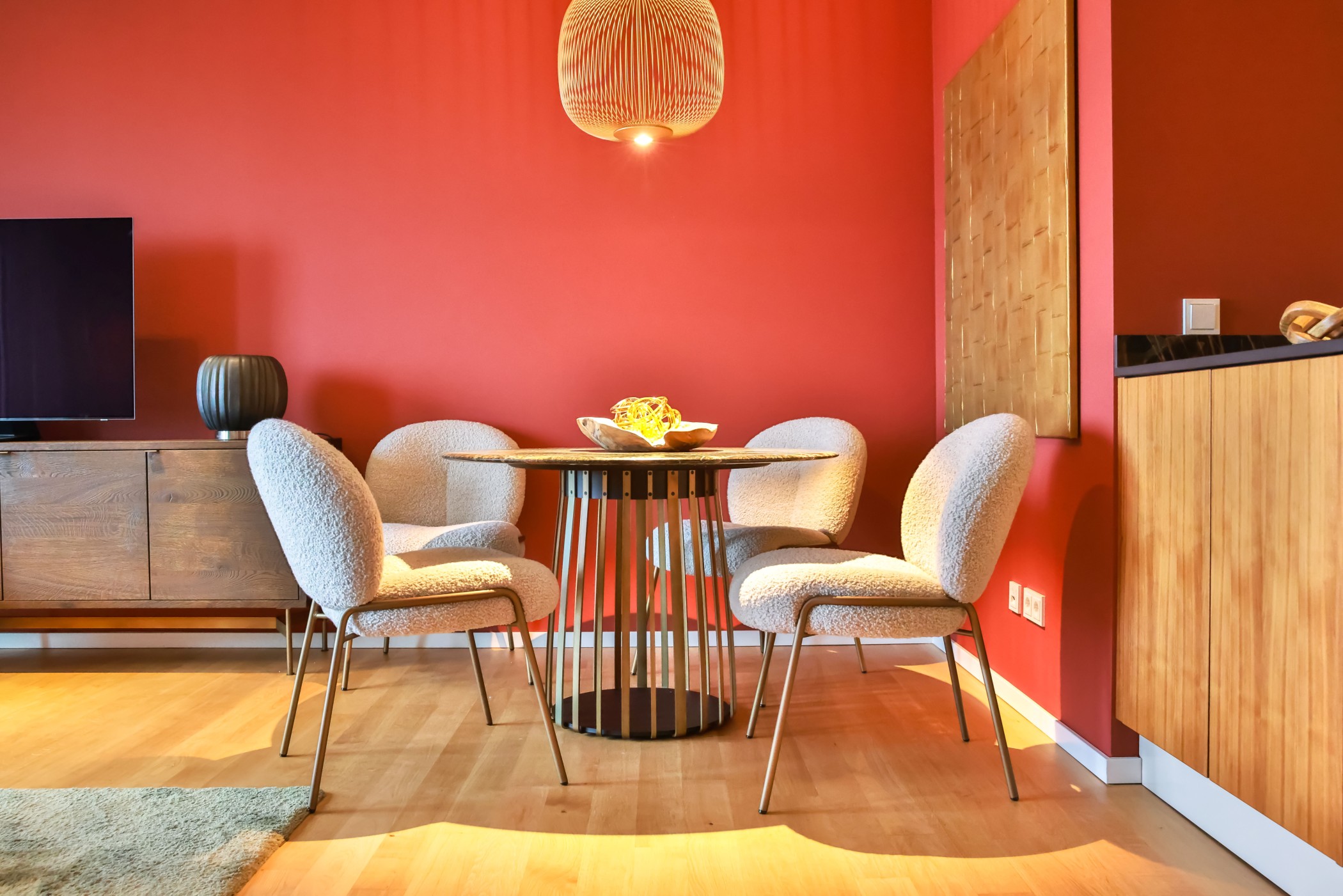 Essbereich mit rundem Tisch und vier gepolsterten Stühlen vor roter Wand im WIN WIN Medienhafen Düsseldorf