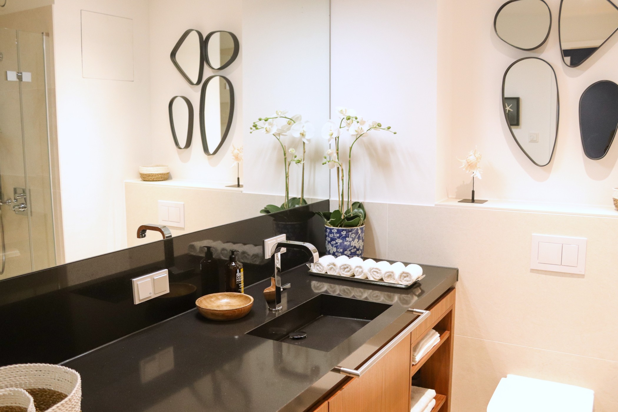Modernes Designerbad einer Luxuswohnung im WIN WIN Düsseldorf mit schwarzer Steinwaschtischplatte, Holzfronten, Orchideen und stilvollen Spiegelakzenten