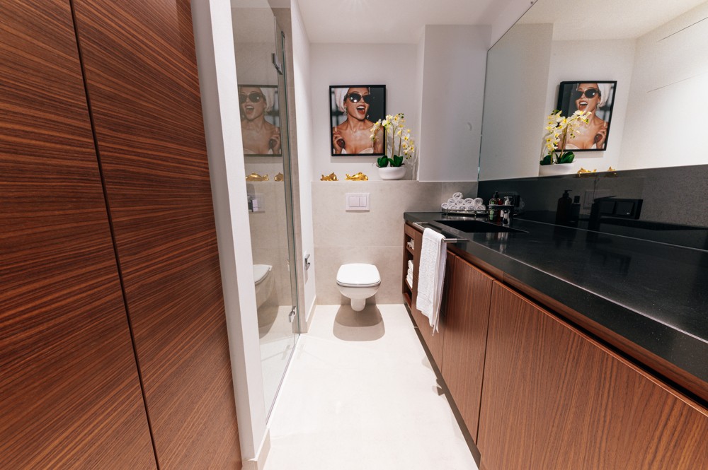 Modernes Badezimmer einer WIN WIN Wohnung im Medienhafen Düsseldorf mit dunkler Waschtischplatte, Glasdusche und stilvollen Deko-Elementen.