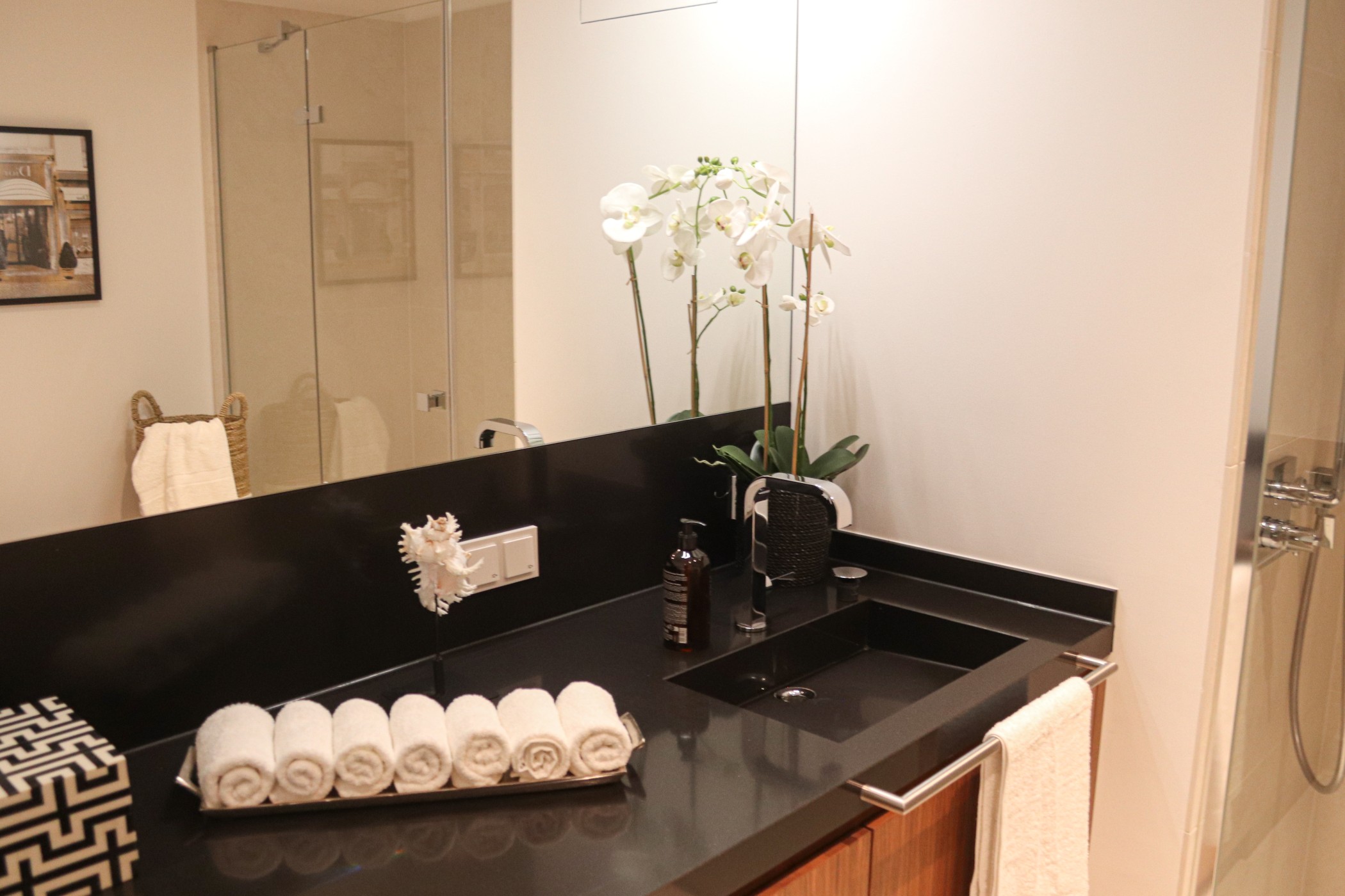 Modernes Designerbad einer Luxuswohnung im WIN WIN Düsseldorf mit schwarzer Steinwaschtischplatte, Holzfronten, Orchideen und stilvollen Spiegelakzenten