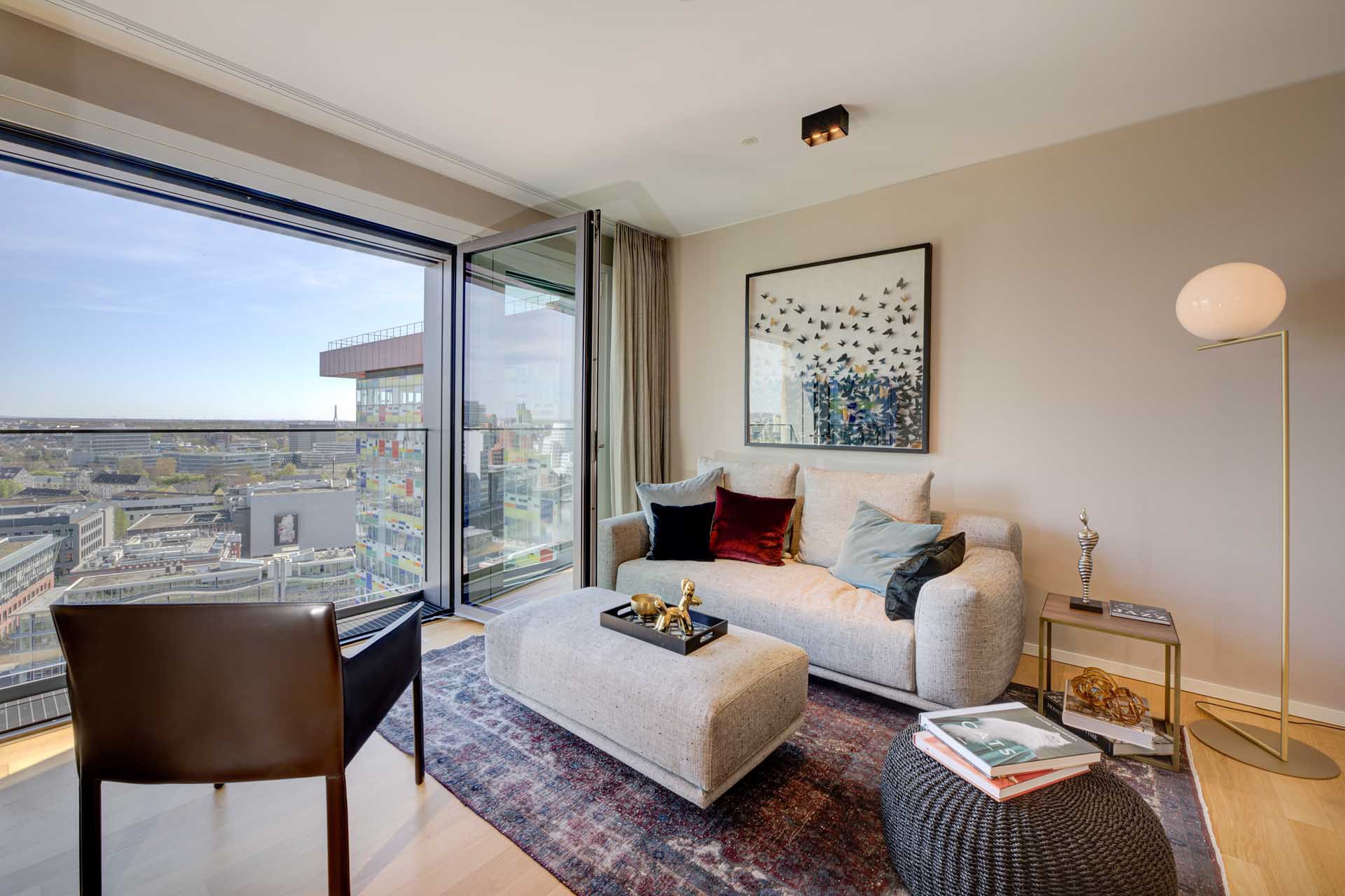 Wohnzimmer mit Sofa und bodentiefen Fenstern mit Blick über Düsseldorf – Luxuswohnung Typ V im Medienhafen kaufen