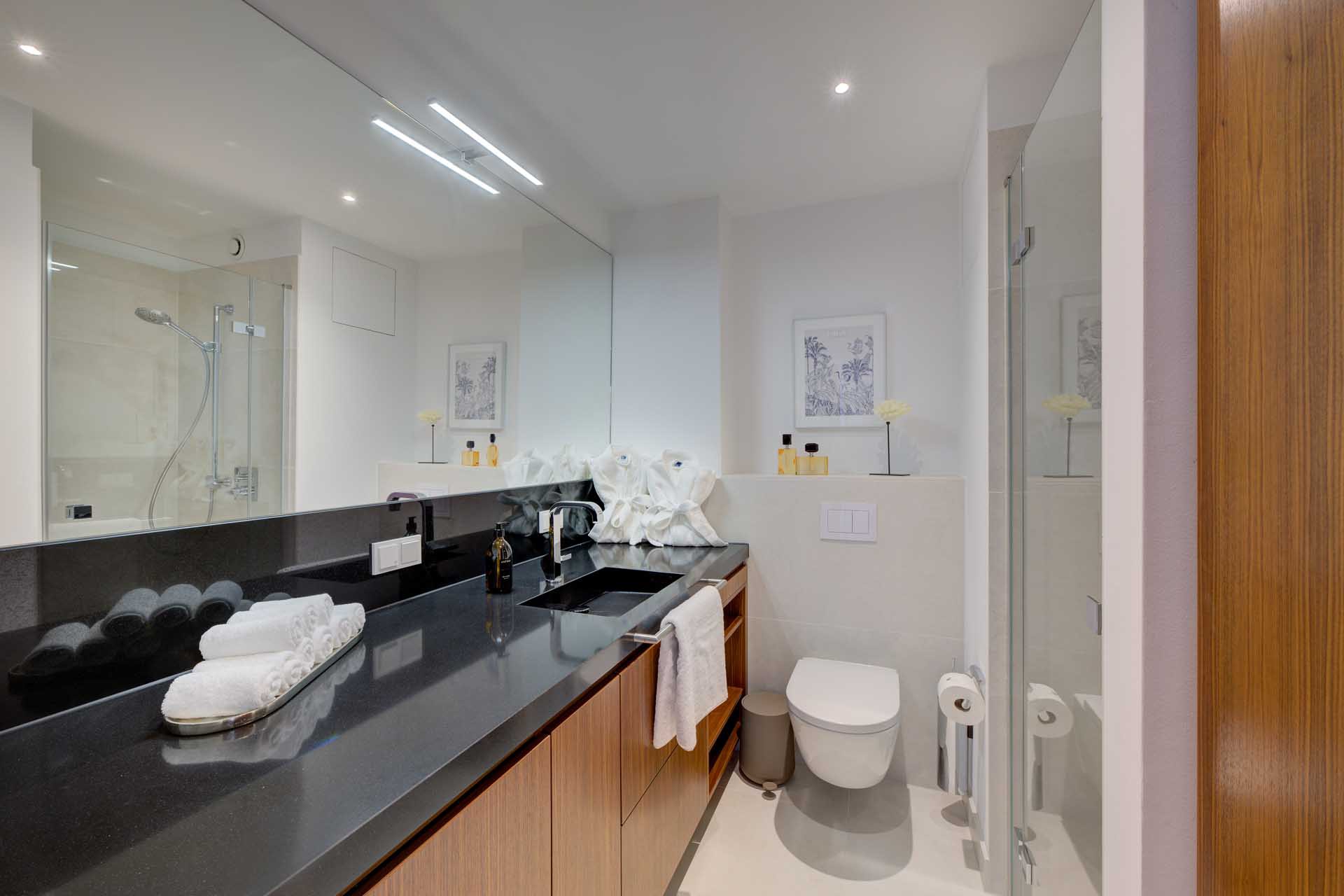 Modernes Badezimmer mit Dusche, schwarzer Waschtischplatte und großem Spiegel – Luxuswohnung Typ U im Medienhafen Düsseldorf kaufen