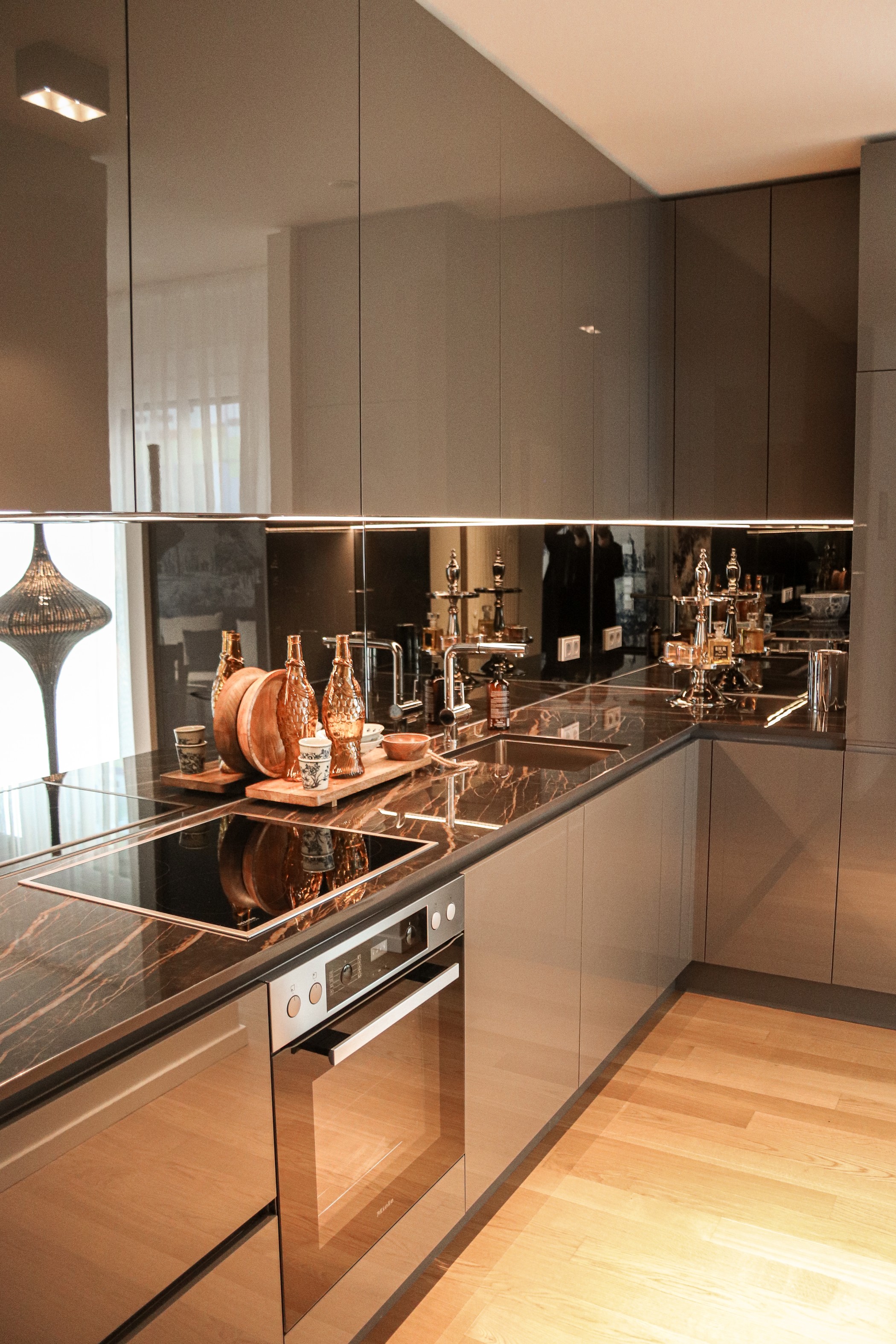 Hochwertige Designküche mit grauen Hochglanzfronten, dunkler Steinarbeitsplatte, Spiegelspritzschutz und eleganter Ausstattung in einer Luxuswohnung im WIN WIN im Düsseldorfer Medienhafen.