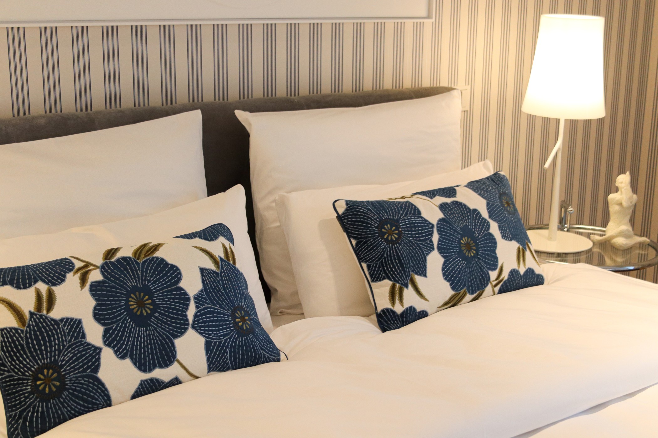 Dekoratives Schlafzimmerdetail mit weißen Kissen und blauen Blumenpolstern im WIN WIN im Düsseldorfer Medienhafen
