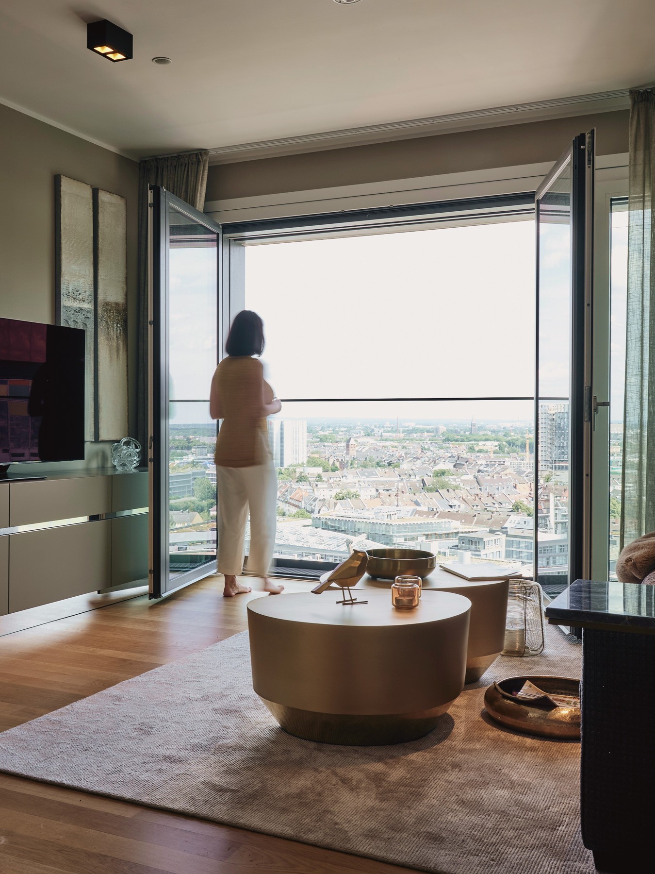 Frau steht in einer WIN WIN Wohnung im Medienhafen Düsseldorf an der geöffneten Panoramafront und blickt über die Stadt.
