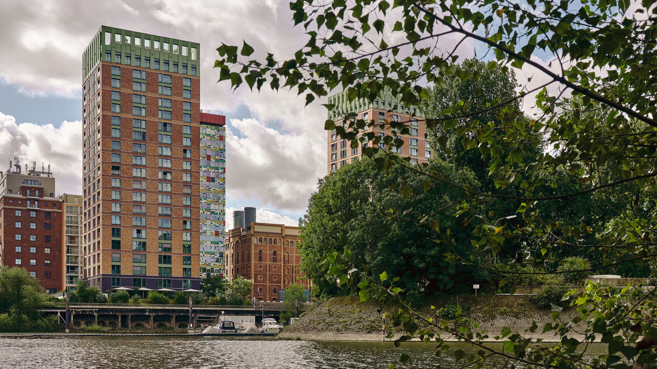 Blick auf die WIN WIN Türme im Medienhafen Düsseldorf, gesehen vom Hafenbecken und eingerahmt von Bäumen im Vordergrund.