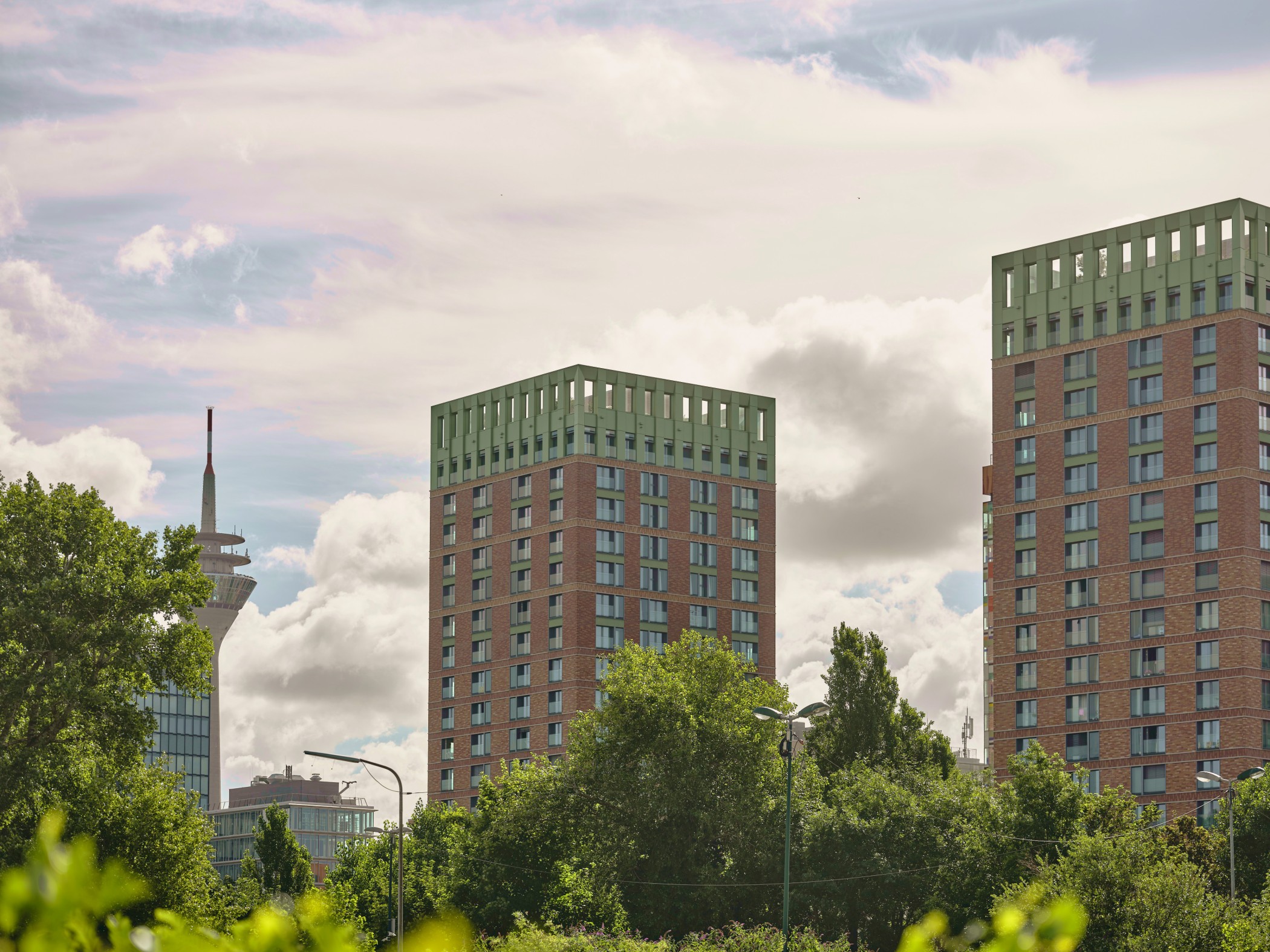 Blick auf die WIN WIN Türme im Medienhafen Düsseldorf mit dem Rheinturm im Hintergrund über einer grünen Baumlandschaft.