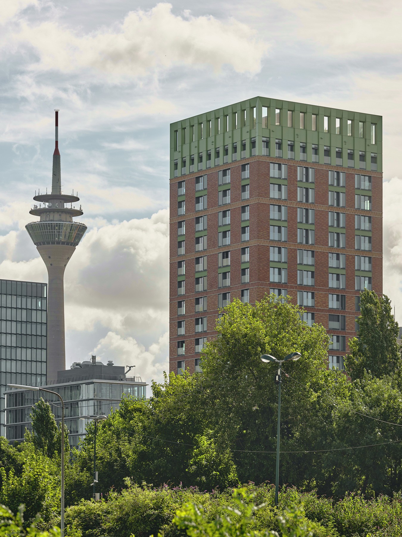 Blick auf die WIN WIN Türme im Medienhafen Düsseldorf mit dem Rheinturm im Hintergrund über einer grünen Baumlandschaft.