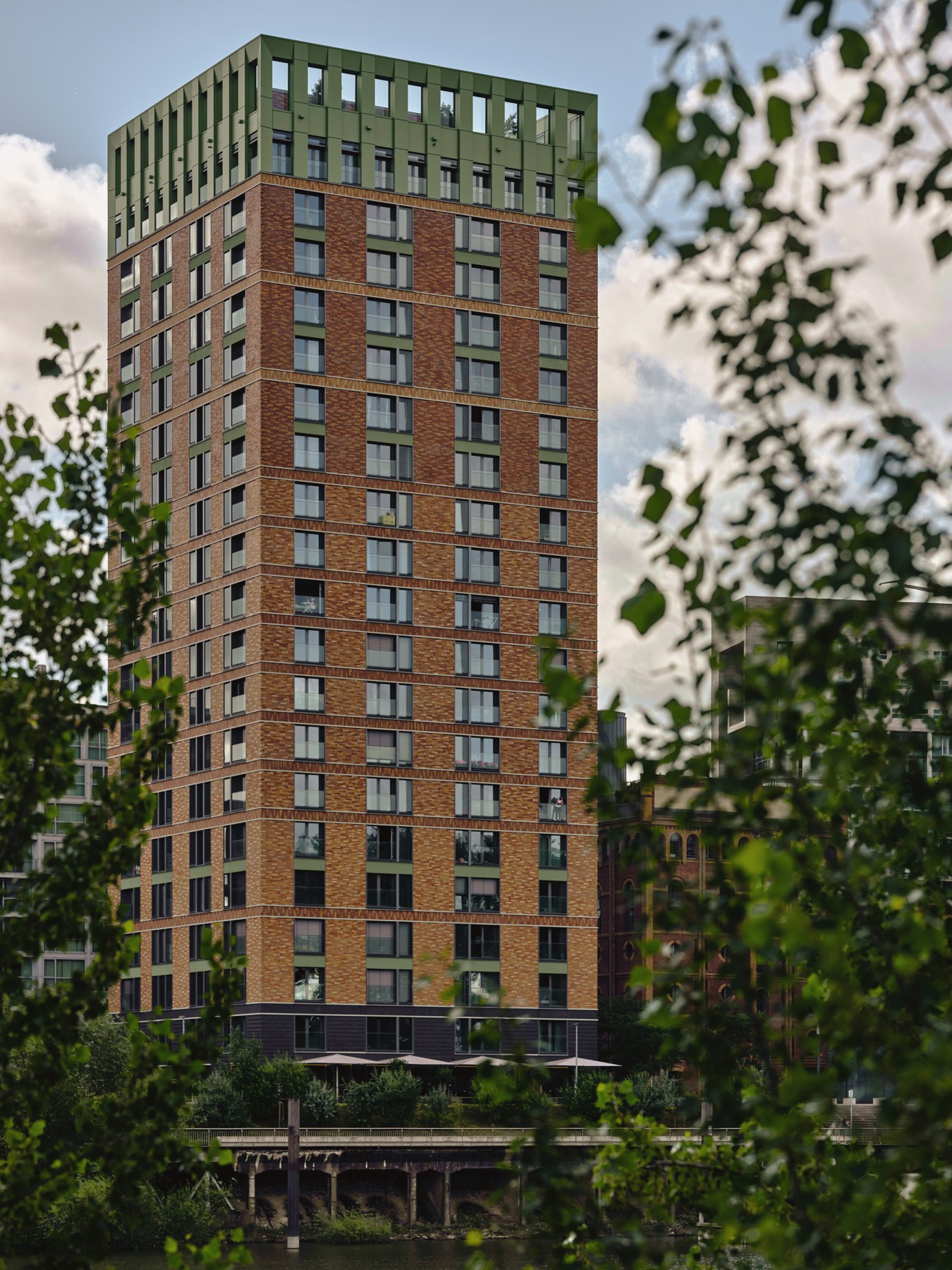 Blick auf die WIN WIN Türme im Medienhafen Düsseldorf, eingerahmt von dichter grüner Ufervegetation am Hafenbecken.