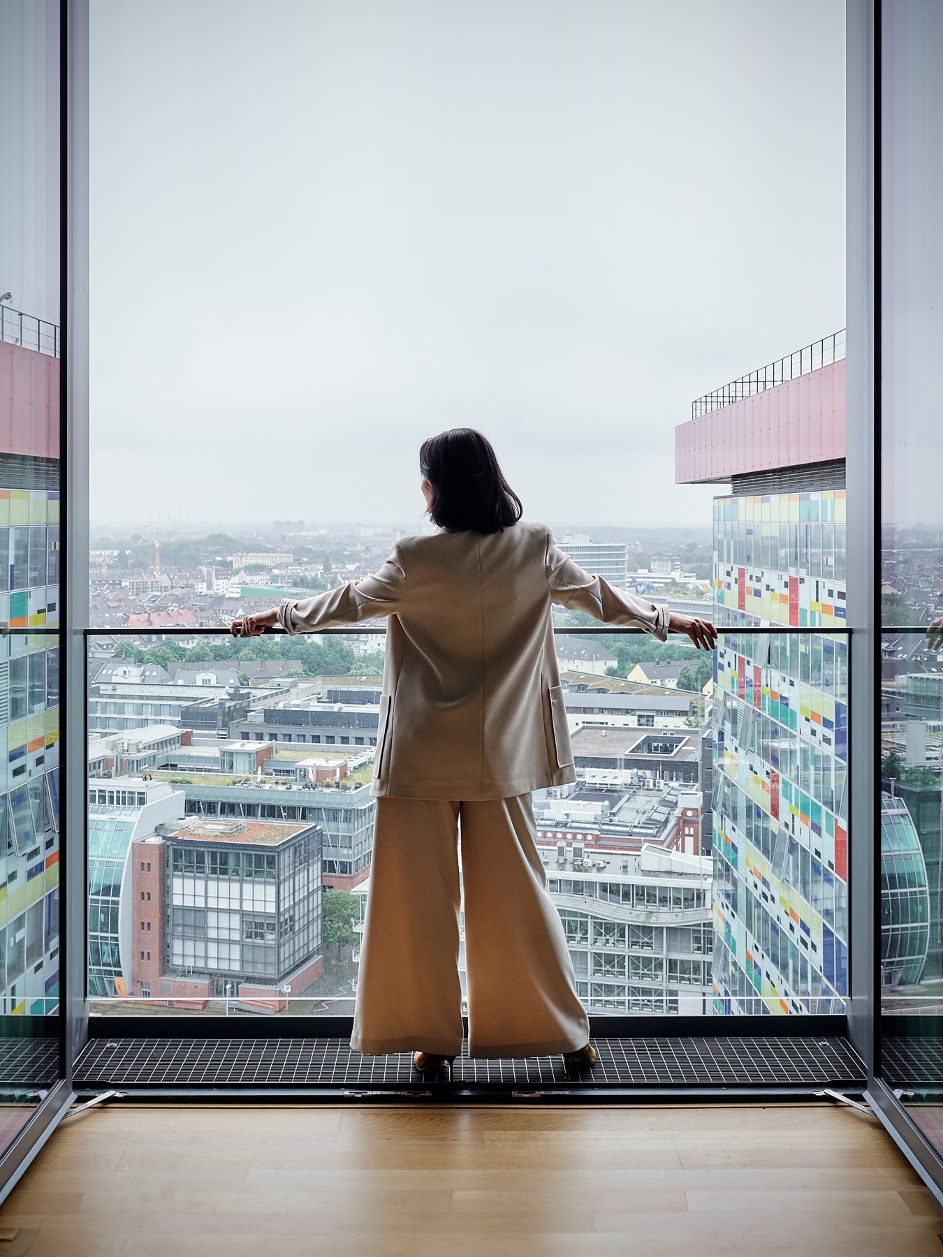 Frau steht in einer WIN WIN Wohnung im Medienhafen Düsseldorf an der geöffneten Panoramafront und blickt über die Stadt.